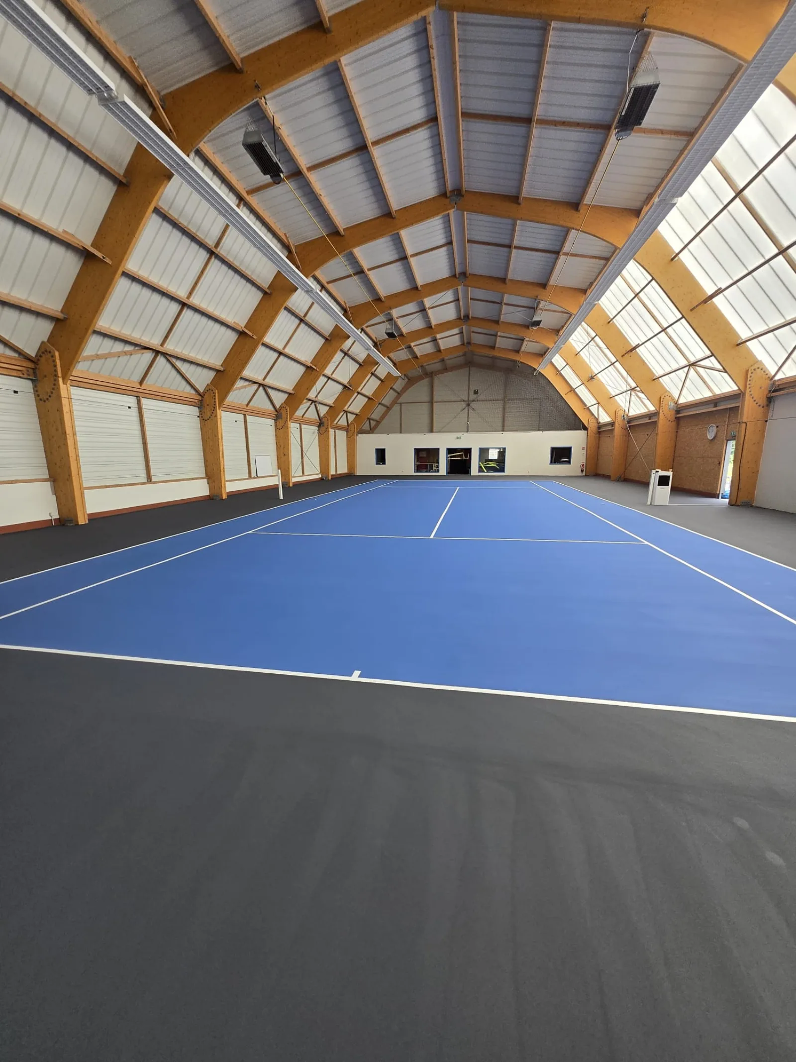 Court de tennis intérieur bleu sous charpente bois lamellé-collé