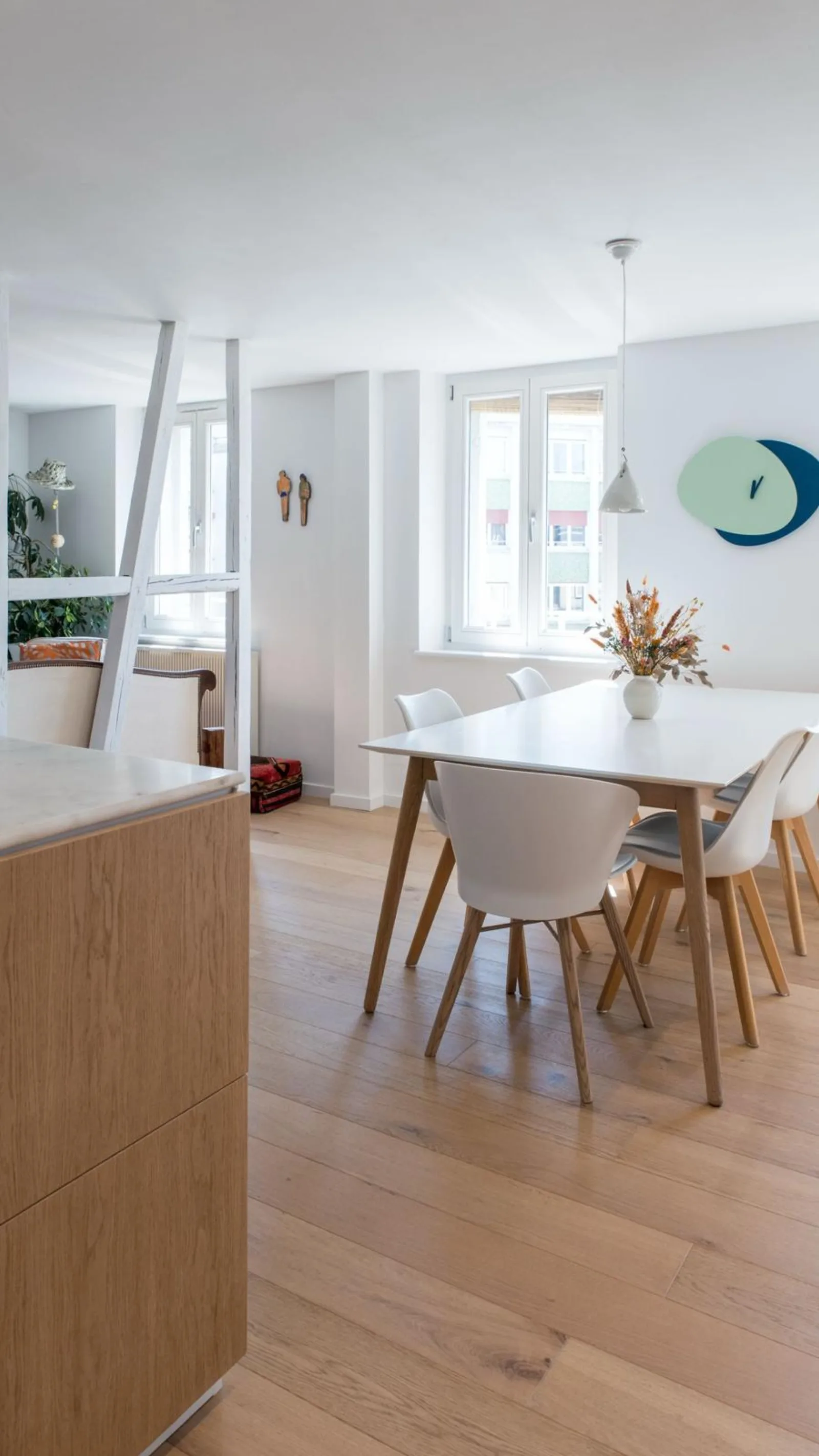 Salle à manger blanche avec table bois et chaises design, fenêtres pans coupés
